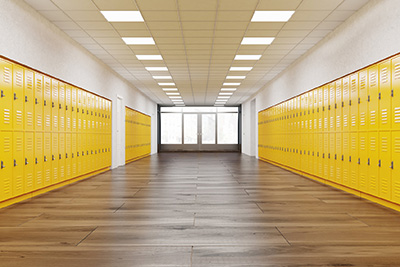 An empty school hallway lined with bright yellow lockers on both sides, leading to a window at the end that illuminates the space with natural light. The floor is wooden, and the ceiling has fluorescent lights, creating a clean and orderly educational environment.