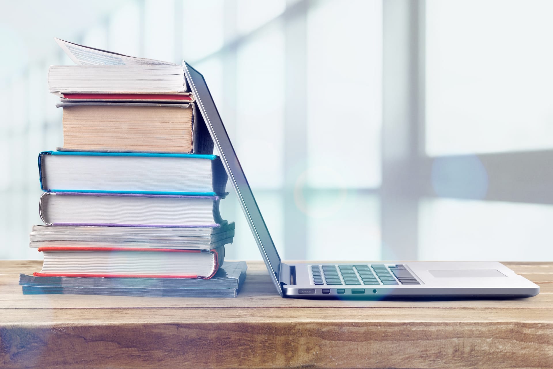 Stack of books with laptop on wooden table