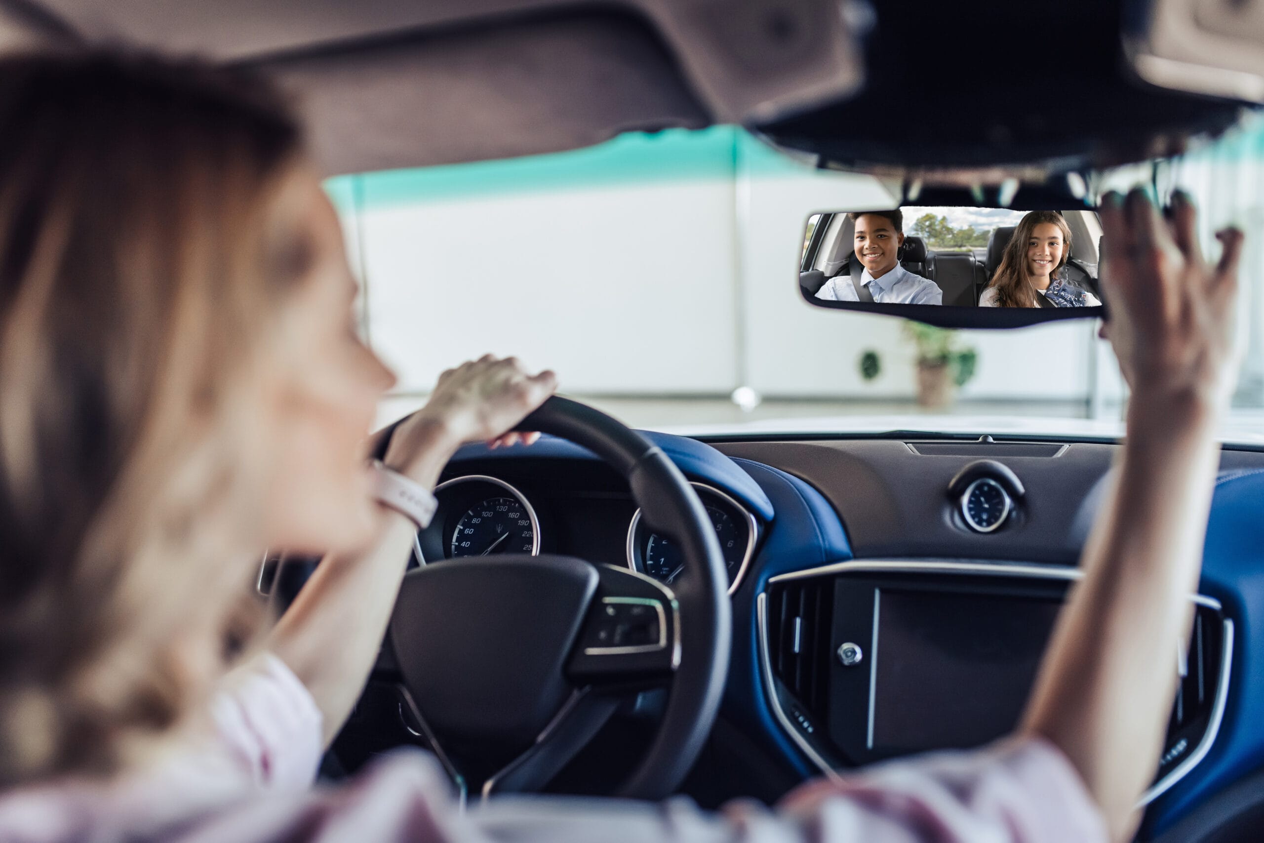 An adult driving children to school while looking in the rear view mirror